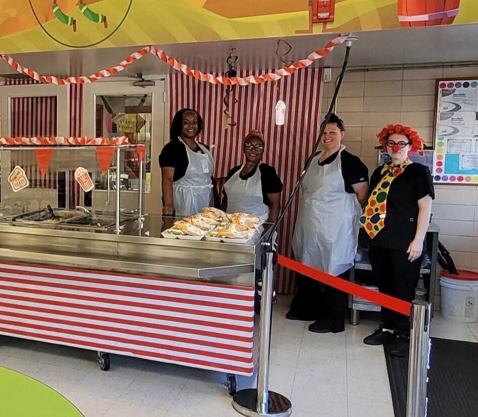 Four cafeteria workers, one of whom is dressed as a clown