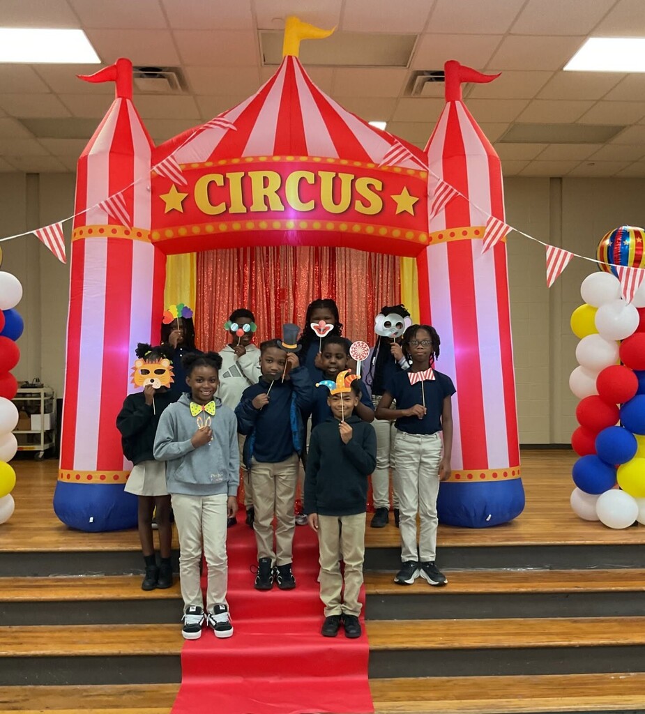 Students holding masks and hats while standing in front of an inflatable circus tent