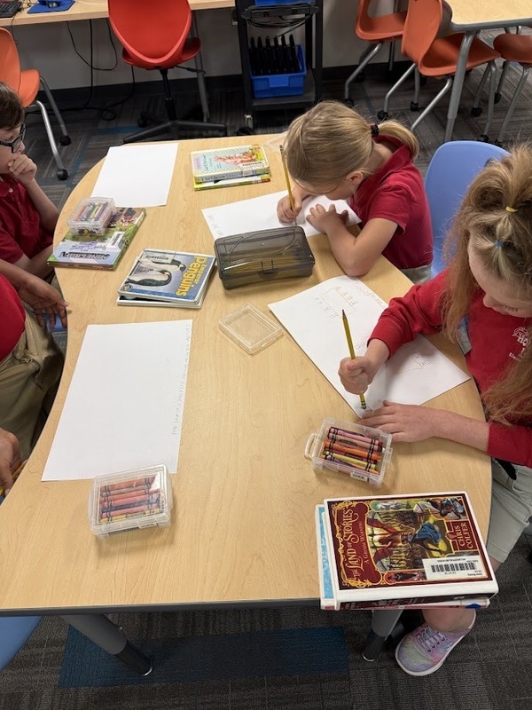 students writing and drawing out predictions at a table in the library
