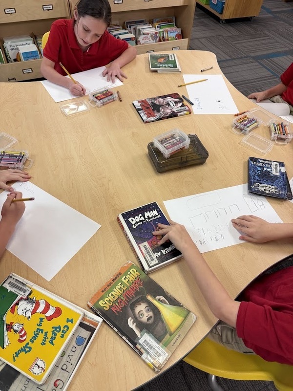 students writing and drawing out predictions at a table in the library
