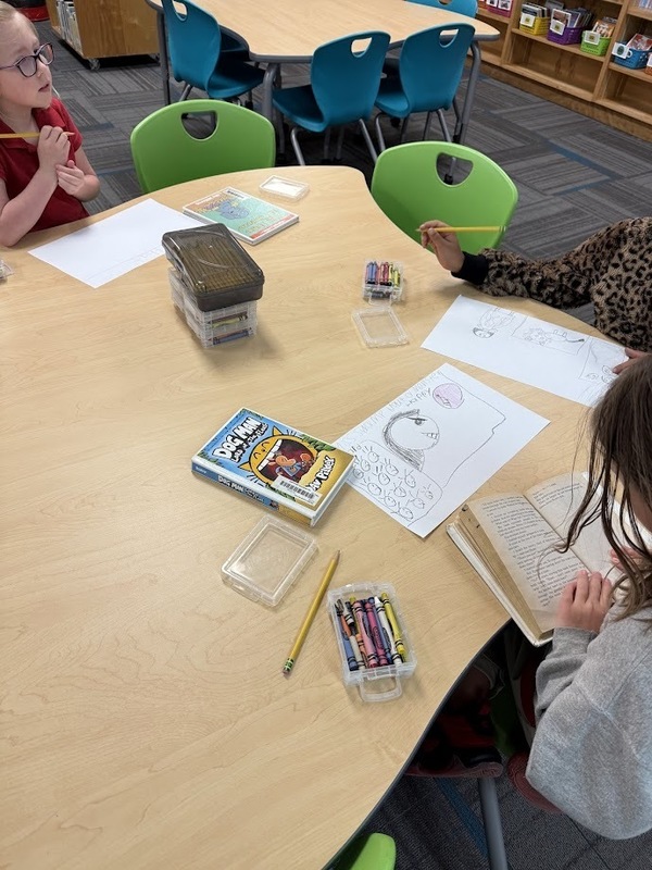 students writing and drawing out predictions at a table in the library