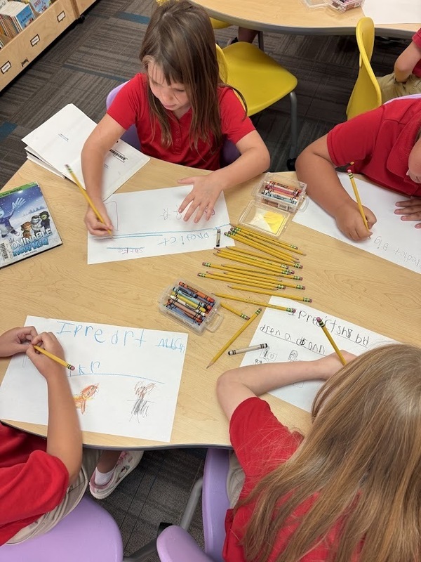 students writing and drawing out predictions at a table in the library