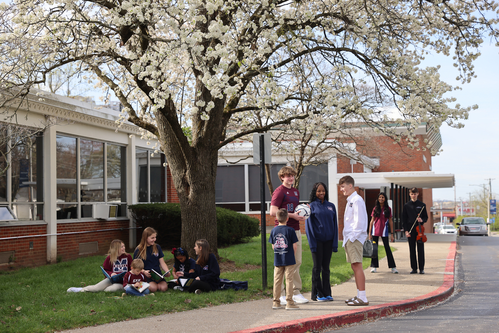 Model students standing at the front of the school under a blooming tree