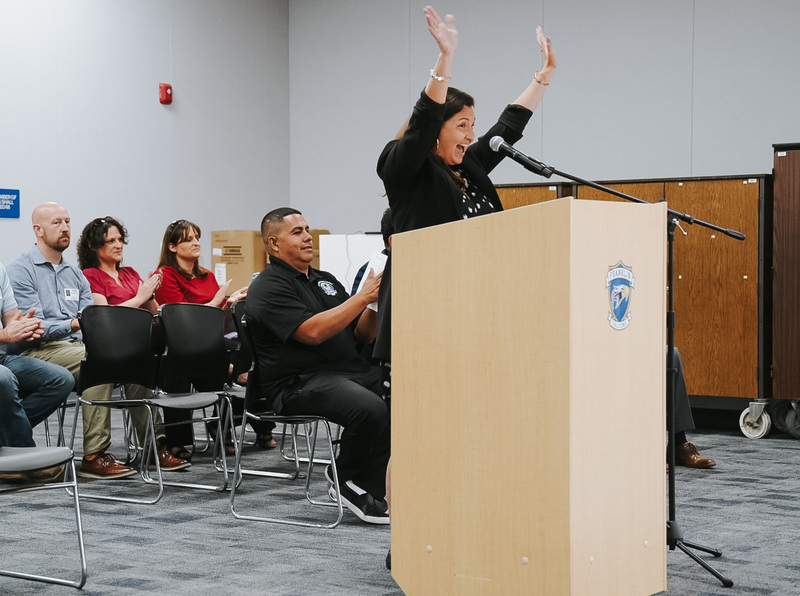 Excited woman raises hands at podium while speaking
