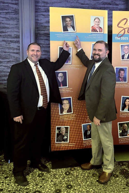 Two men pointing at woman's photo on banner behind them