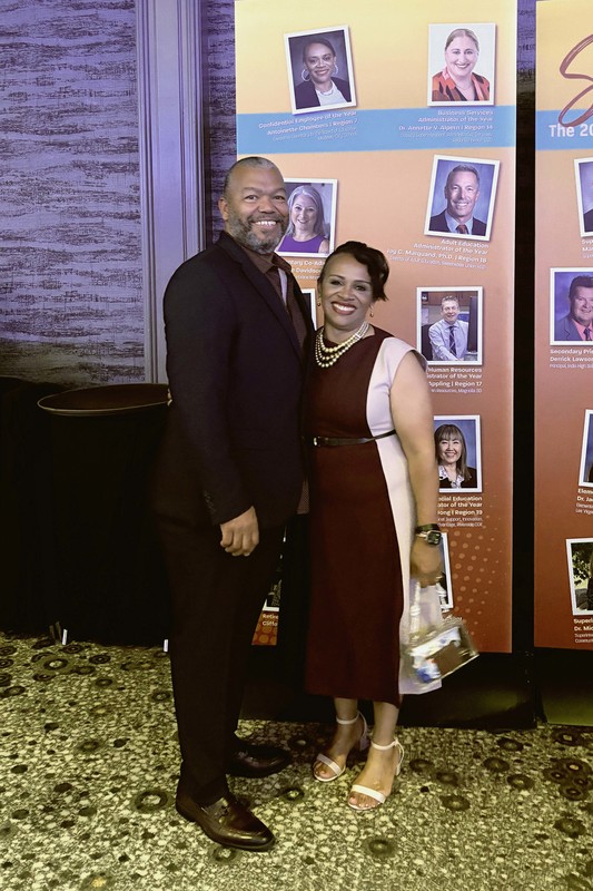 A man and woman in formal attire posing in front of three banners with award winners printed on them