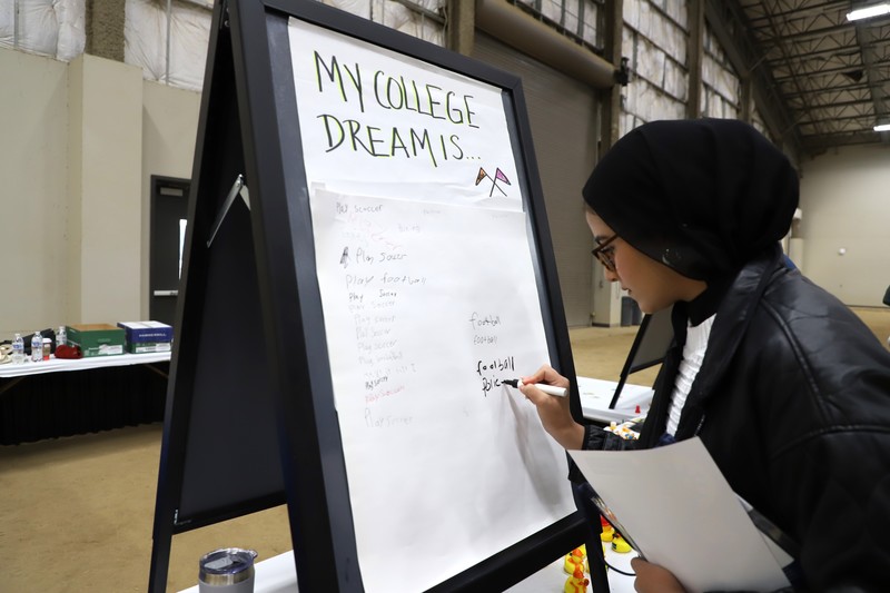 Student writes what their college dream is on a dream board at the event.
