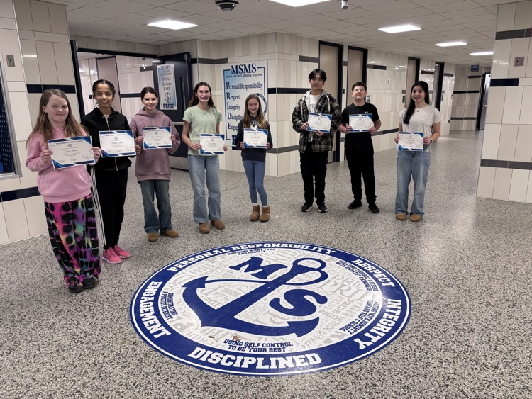 students of the month in the foyer of the school holding their certificates