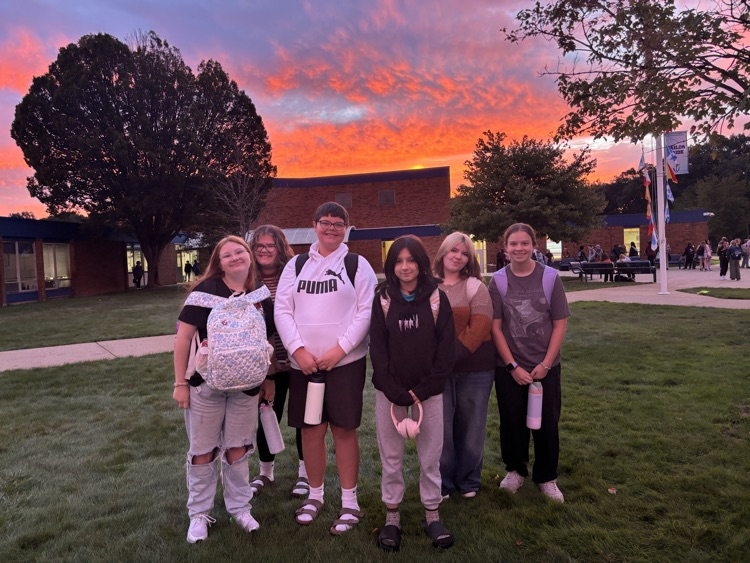 group of students in front of the school with the sunrise in the background 