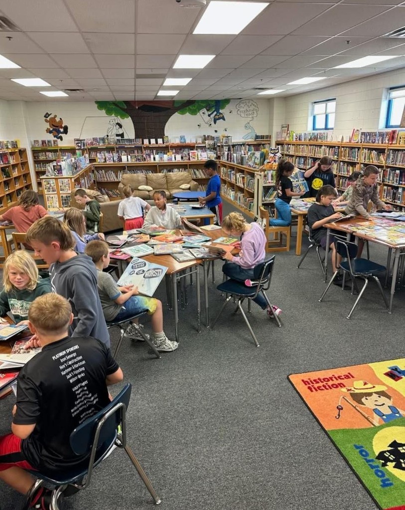 Students at tables silent reading from a stack of books