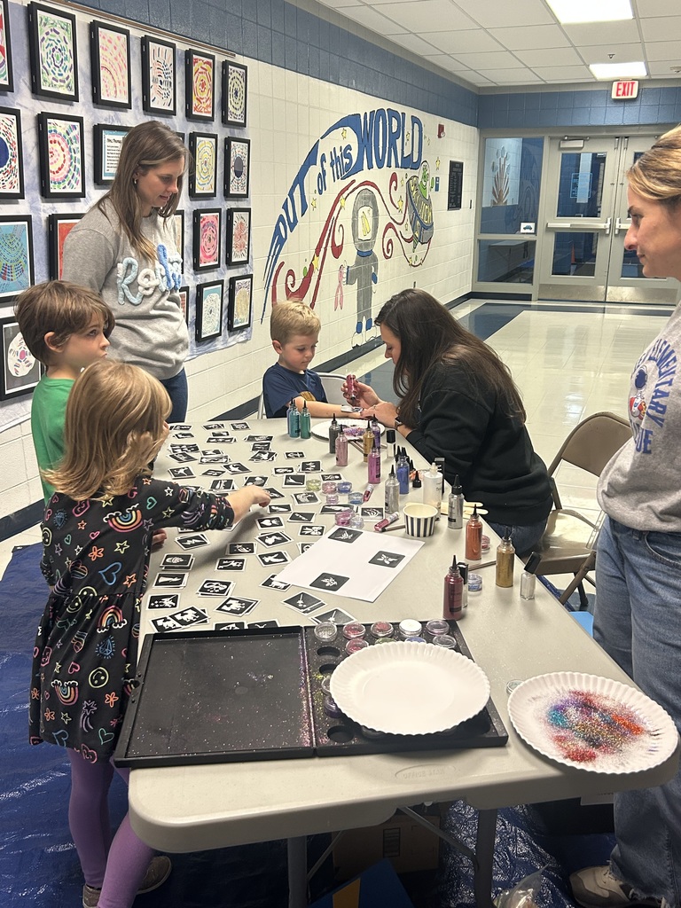 table of students getting glitter tattoes on their arms, teachers looking on