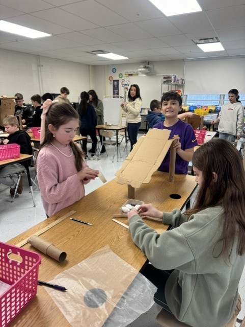 In the STEAM Lab making a sled run. Students had to design an incline that would allow their sled to complete the run and keep their snowman parts and people inside the sled. They measured the distance their sled ran.