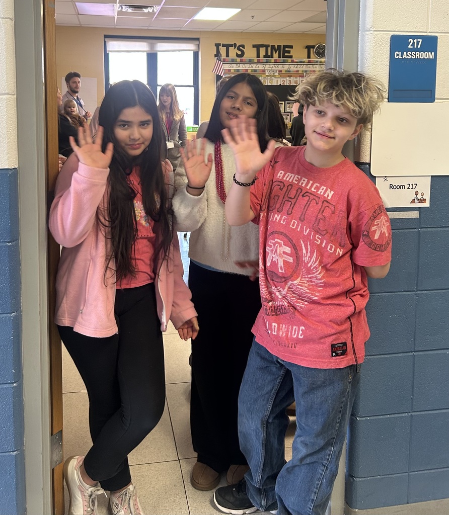 three students standing in doorway waving