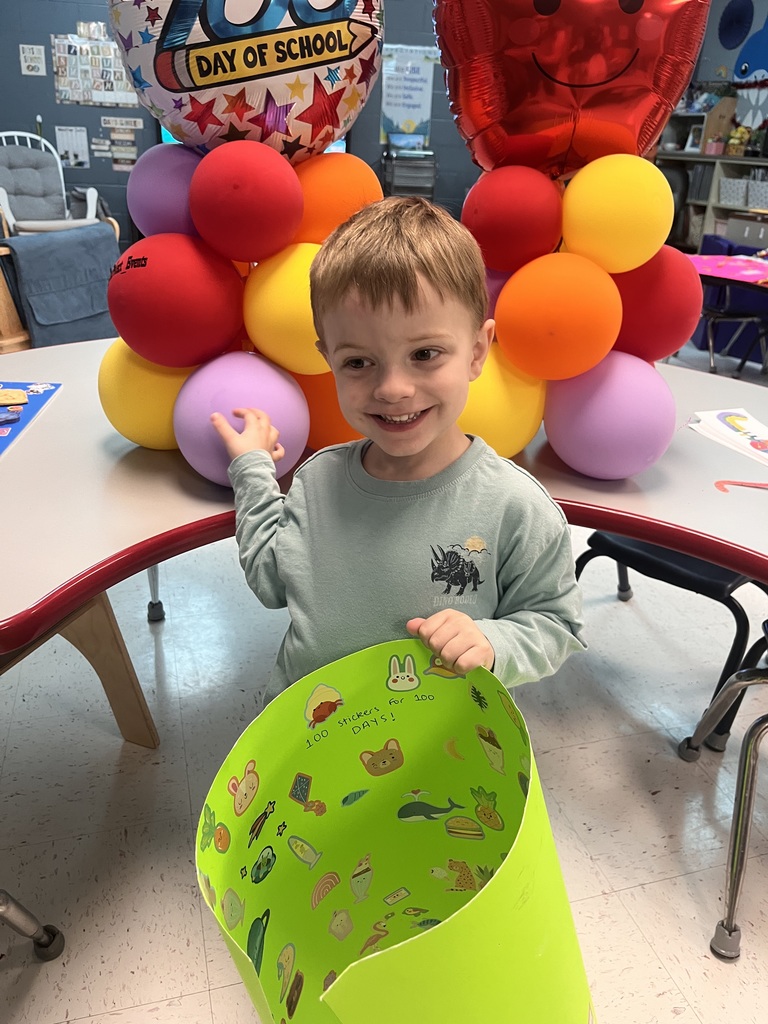 PreK student in front of balloons celebrating 100 days with a poster project!