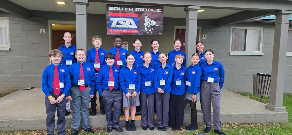 Group of students with blue shirts standing under a South Middle TSA banner