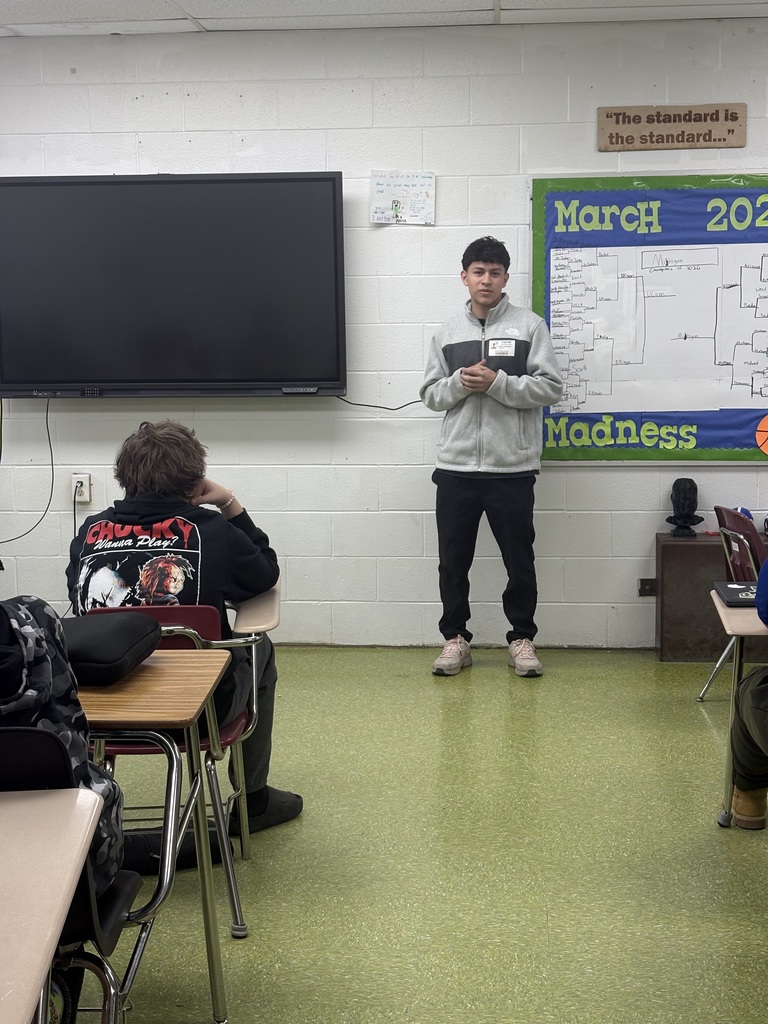 A student standing in the front of the classroom talking to his classmates