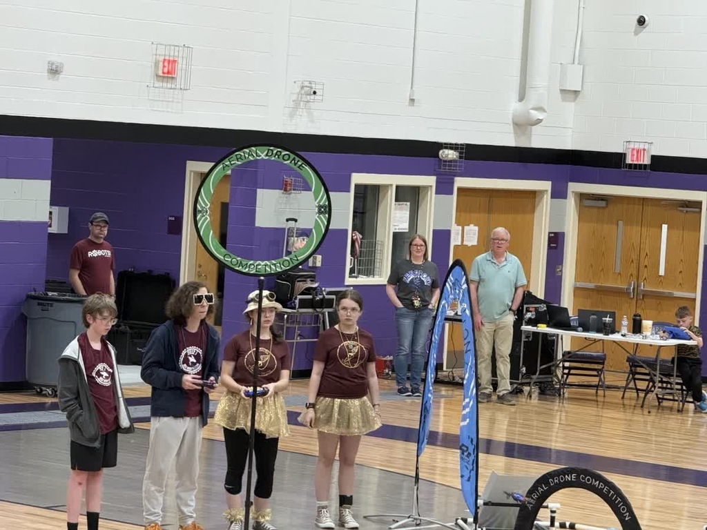 4 students standing in a gym controlling a drone through an obstacle course