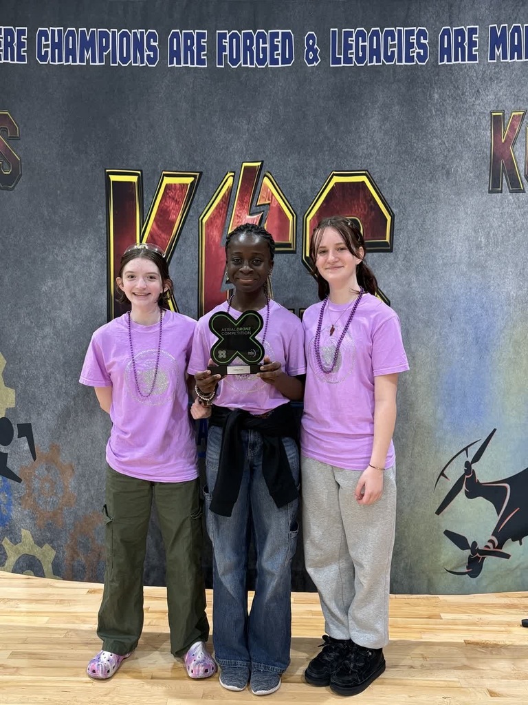 3 students holding a trophy in front of a banner that says Champions are forged 
