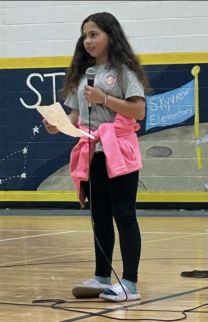 4th grade student standing with microphone reading her speech on how the Source helps her
