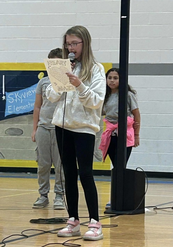 4th grade student standing with microphone reading her speech on how the Source helps her