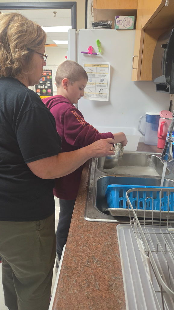 A boy is washing a bowl at the sink. The water is running into the sink and a woman is standing beside the boy.