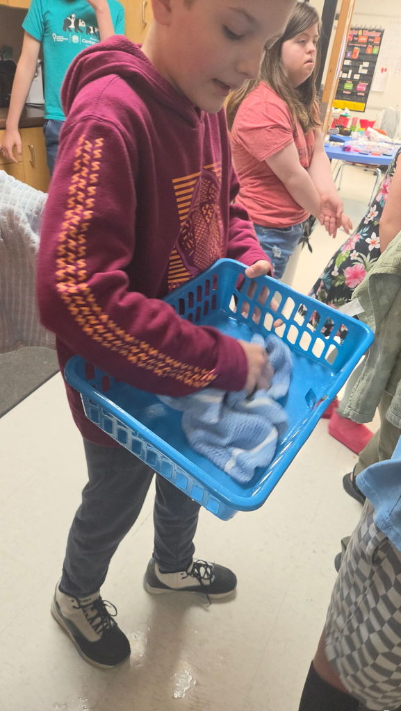 A boy drying a basket with a dish towel. There is a girl in the background.