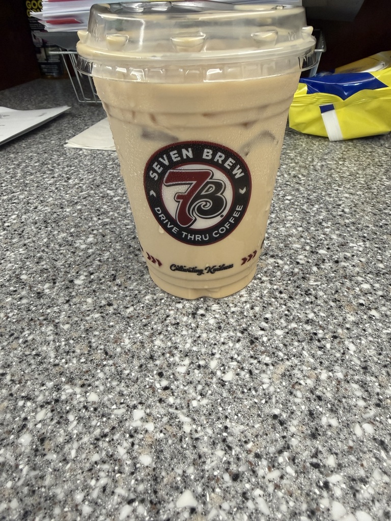 Clear coffee cup filled with an ice coffee the cup says seven brew drive thru coffee on it. This cup is sitting on a counter.