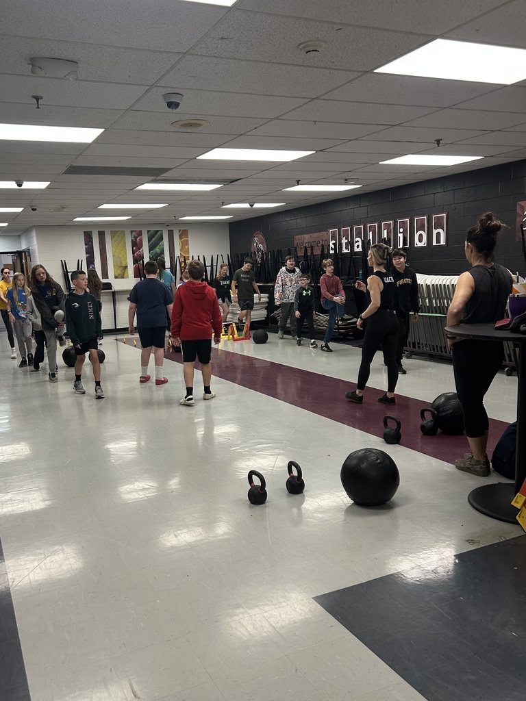 Students are carrying kettle balls and weights while 2 women from Warrior Bodies are directing them.