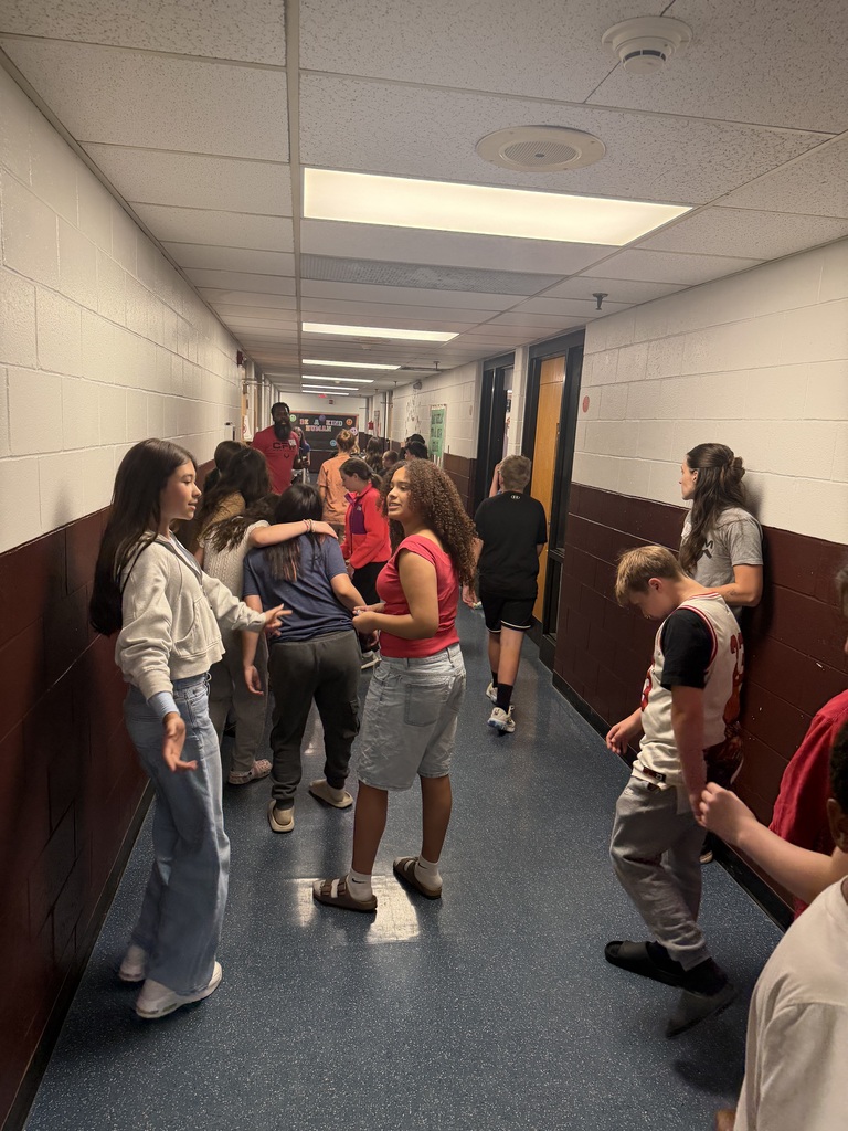Students are in a hallway looking around and there are also 2 adults in the hallway.