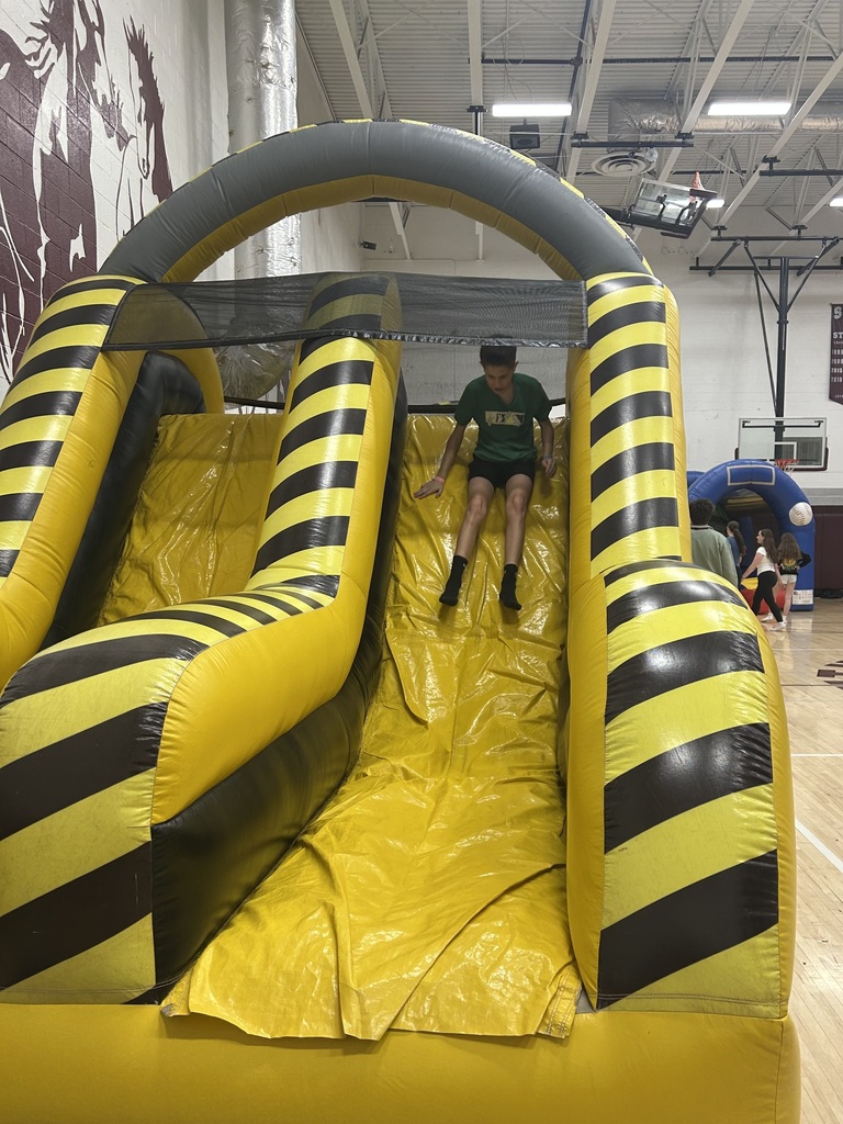 A student coming down an inflatable slide in a gym.