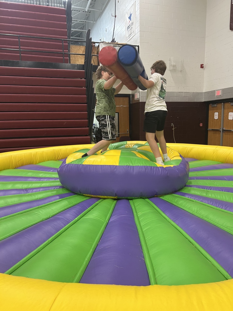 Two boys standing on an inflatable platform with a red and blue foam thing. They are pushing the 2 foam logs together.