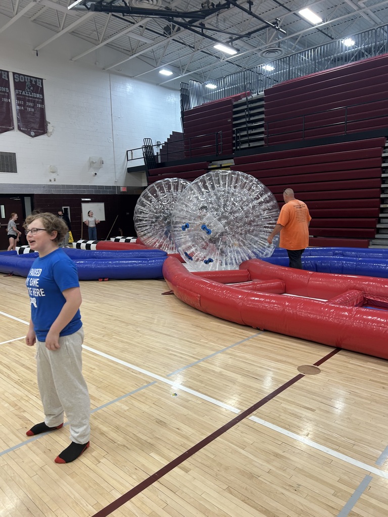 Kids standing in the gym and there are 2 inflatable balls with a red and blue track.