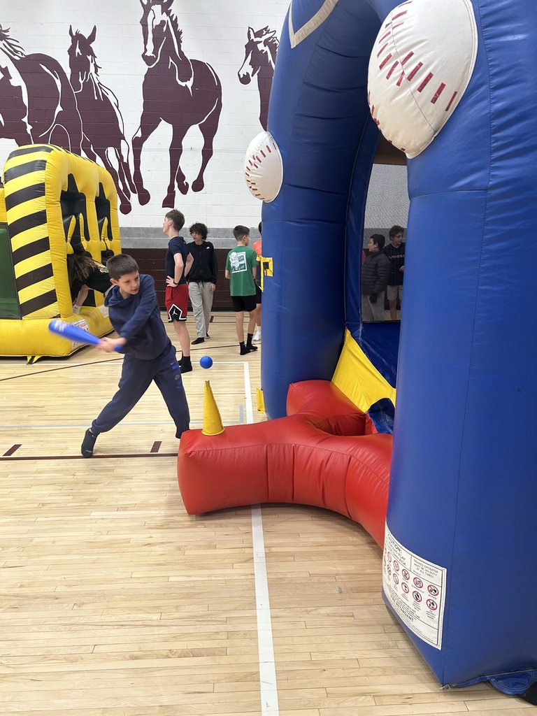 A boy with a bat in a gym swinging at an inflatable blue and red station.