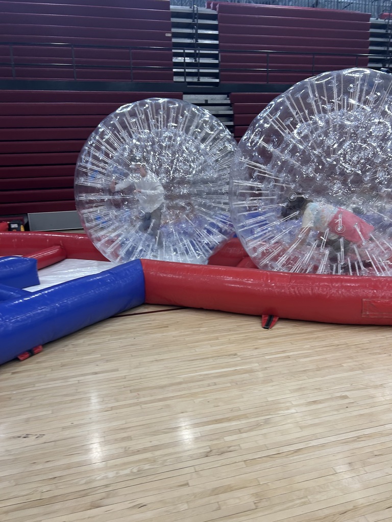 2 students in inflatable balls on an inflatable track that has been set up in a gym.