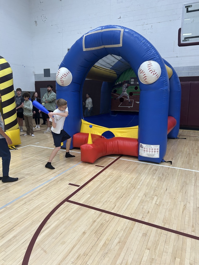 Students in a gym one boy is swinging a bat at an inflatable baseball field.
