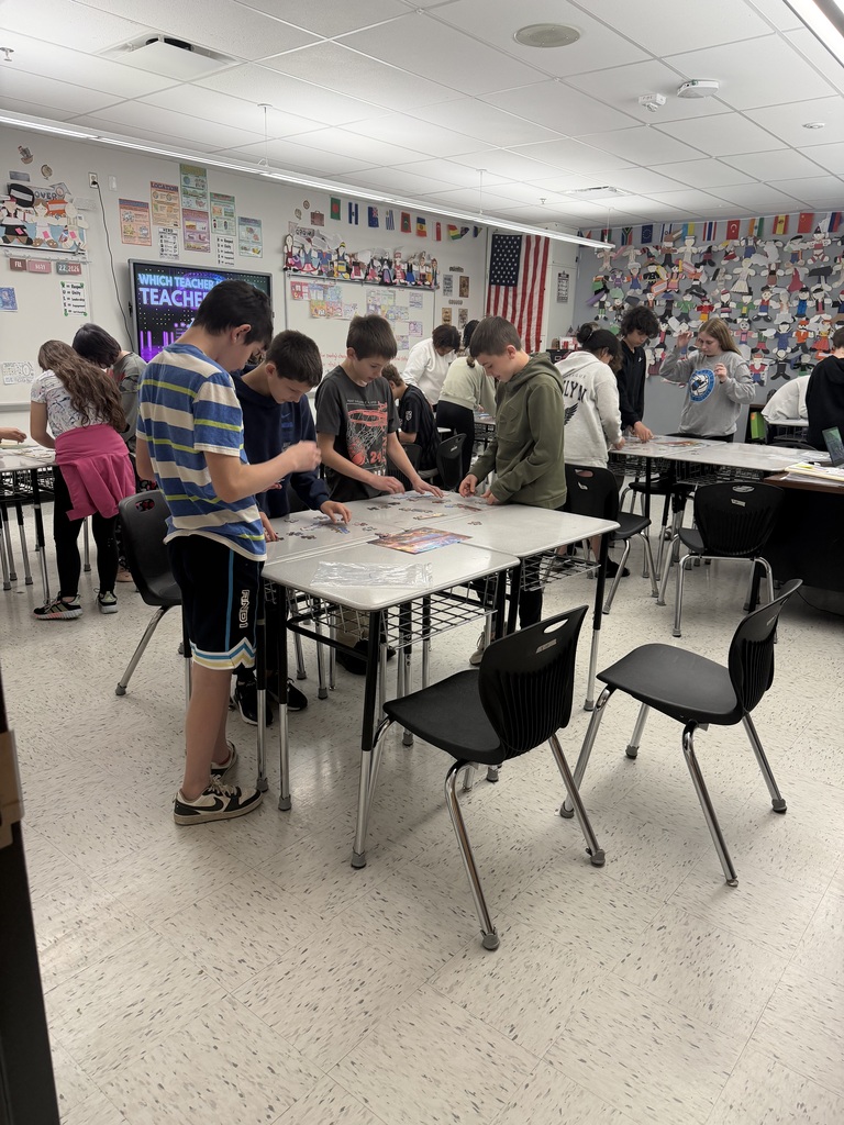 Students in a classroom standing at desks putting puzzles together. 