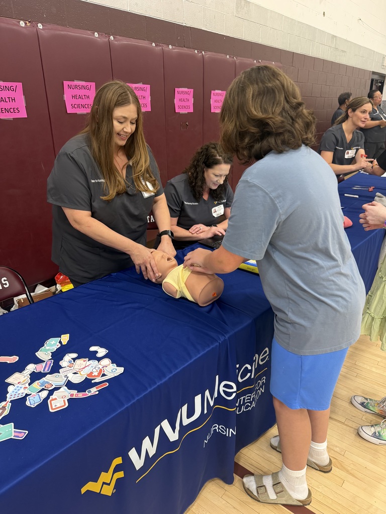 Nurses are showing a group of students how to save a choking baby. They are at a table in a gym.