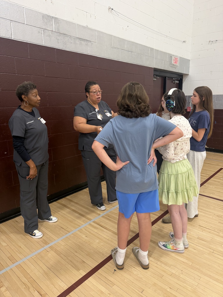 2 nurses are talking to a group of girls in a gym.