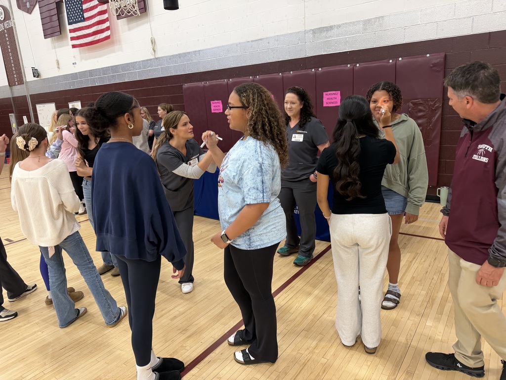 Kids standing in a gym. One girl is getting a light shown in her eyes. There are nurses in the background.