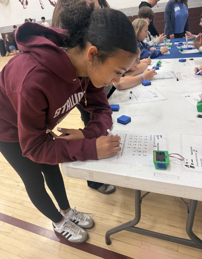 A girl is leaning over a table in a gym writing something.