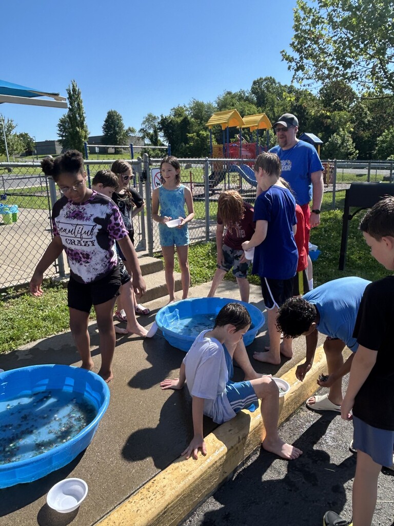 4th grade group of students standing amongst two kiddie pools transferring marbles with thier bare feet