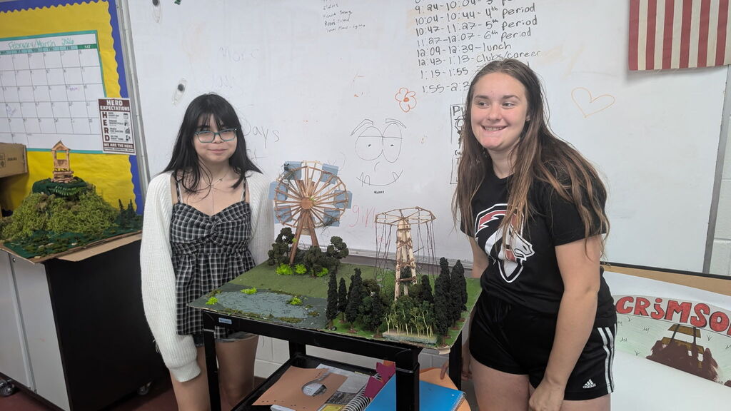 Two girls standing beside a project that appears to be an amusement park. They are in a classroom.