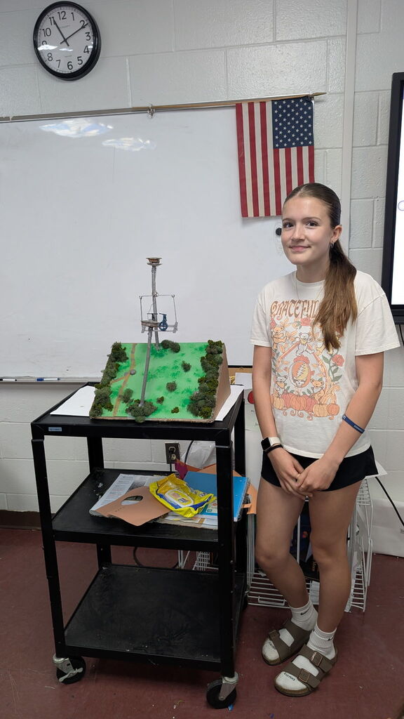 A girl standing beside a project in a classroom.