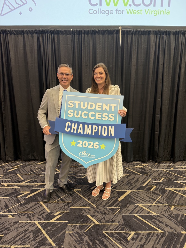 A man in a suit and a woman in a dress holding a sign that says Student Success Champion 2026. 