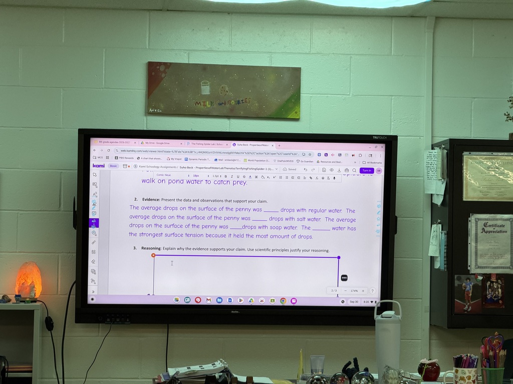 A whiteboard screen in a classroom displaying a Science worksheet. There is a lamp on beside the whiteboard and you can see items sitting on the teacher's desk in front of the whiteboard.