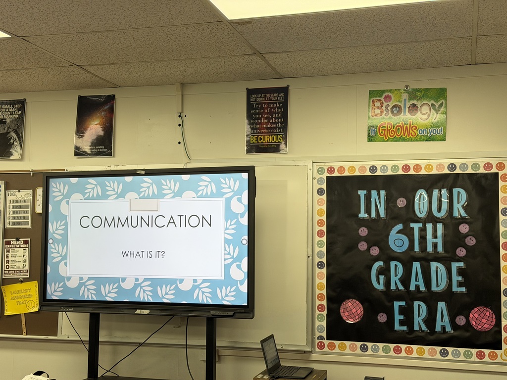 A whiteboard with a blue border and Communication What is it? posted on it. There is a bulletin board to the right of the white board that says In our 6th grade era with 2 red disco balls on it.