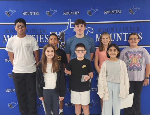 The MMS Students of the month are gathered in front of the MMS Banner for a group photo.