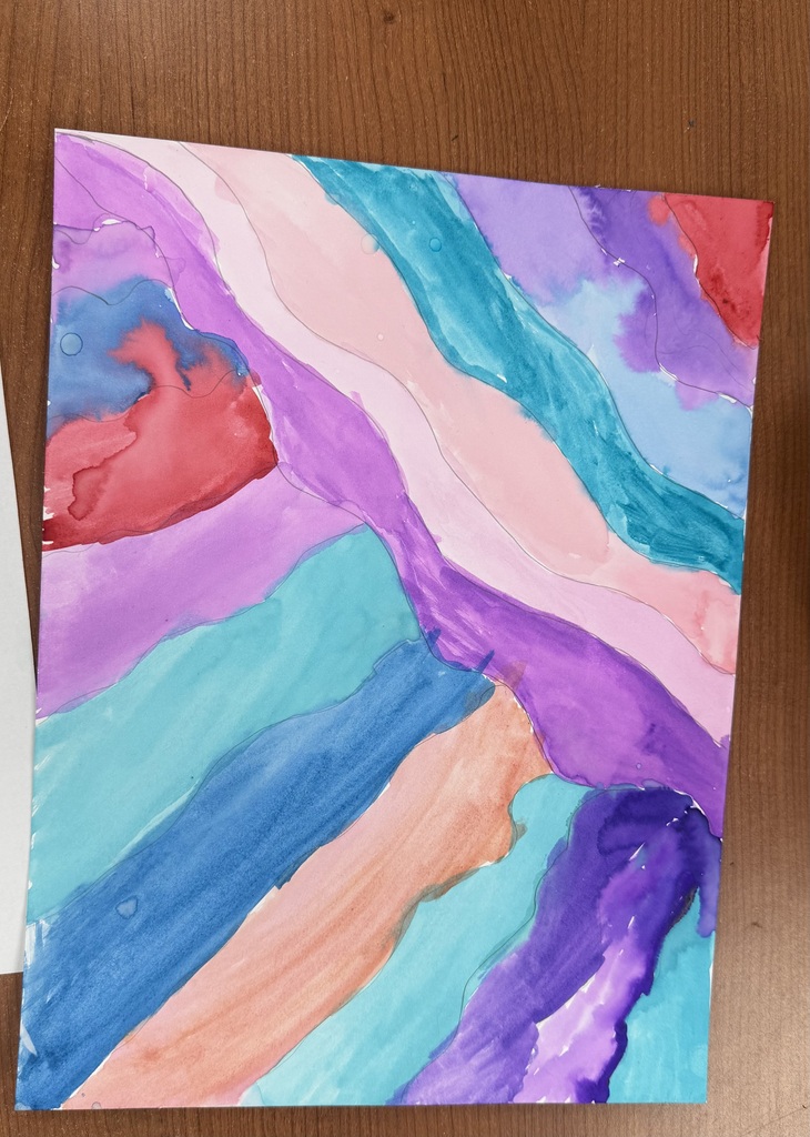 Piece of paper that has been painted red, blue, light blue and purple. It is sitting on a table.