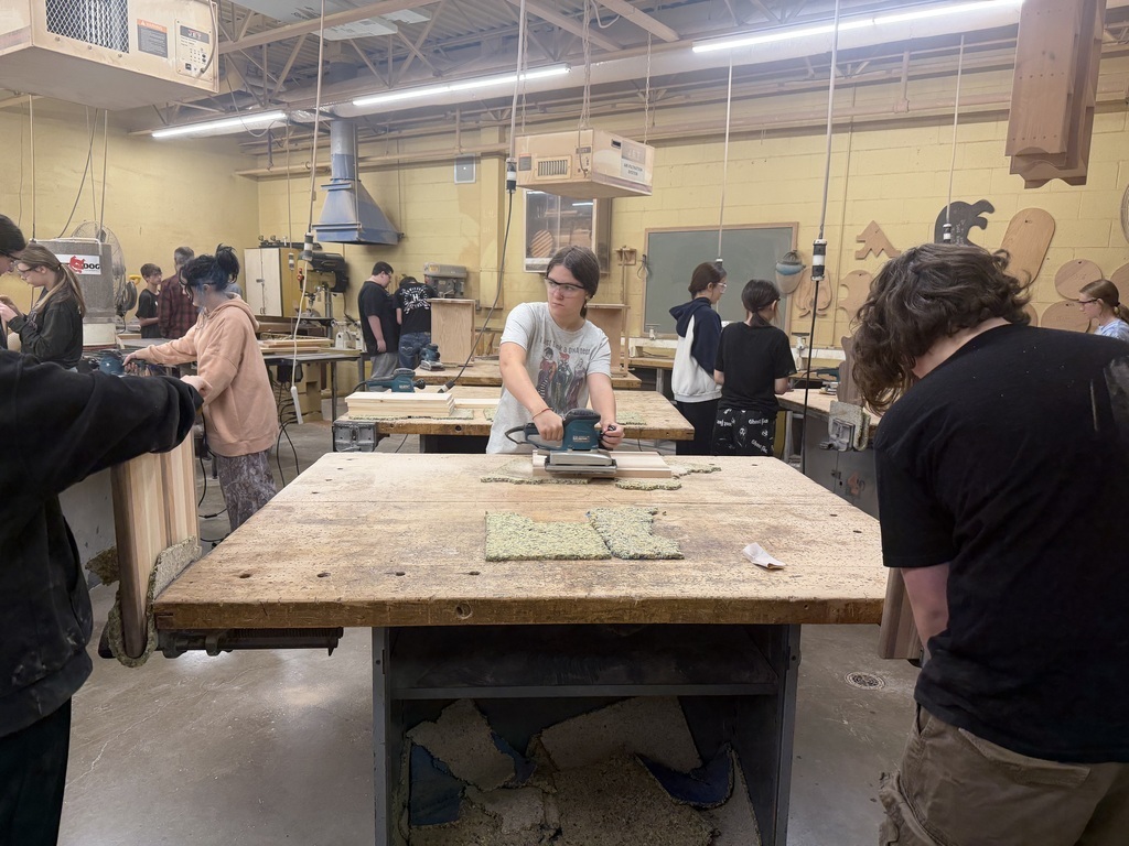 Students are working in a workshop. Some students are sanding and others are facing with their backs to the camera.