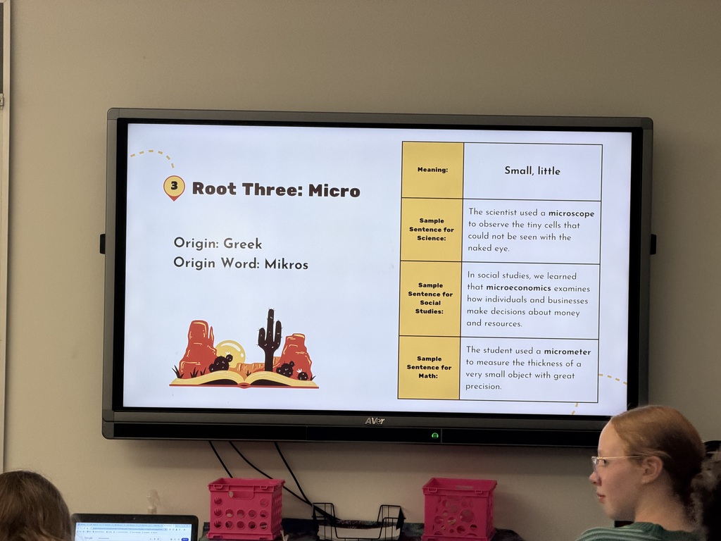 White board in a classroom with a slide about Root Three: Micro. A students head is in the bottom corner of the photo.